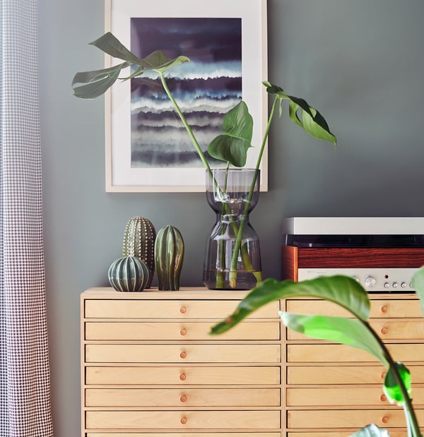 Wood dresser with copper knobs, vases, plant, art, grey wall.