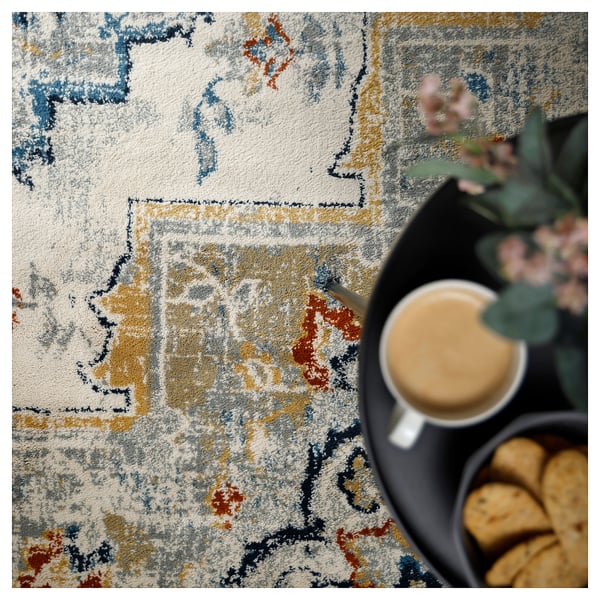 Cream-colored ONSEVIG rug with faded oriental design, tray of pastries, and coffee.