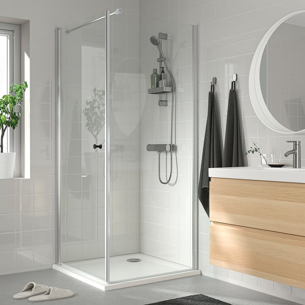 Modern bathroom with glass shower, dark towels, wooden vanity, white & grey tiles, round mirror, potted plant.