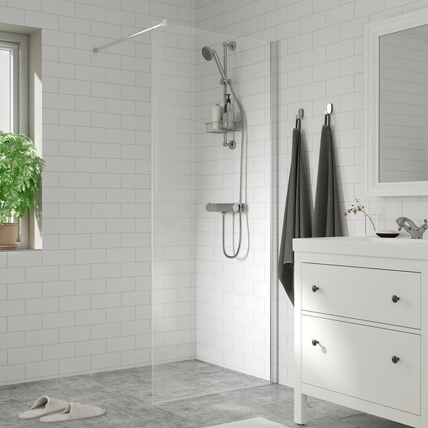 Modern bathroom with white tiles, glass shower, chrome fixtures, grey towels, small sink, mirror, and plant.