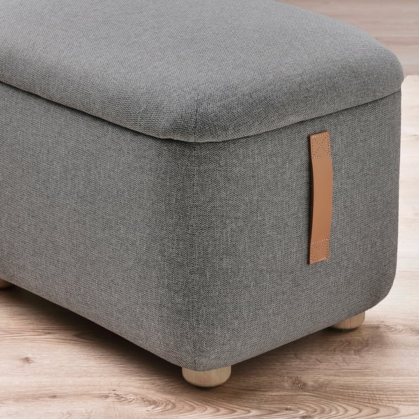 Close-up of modern grey upholstered footstool with sturdy wood legs and leather handle, showcasing quality fabrics and craftsmanship.