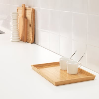 Wooden tray with two white mugs and spoons, set on a white countertop beside wooden cutting boards and a stack of white plates.