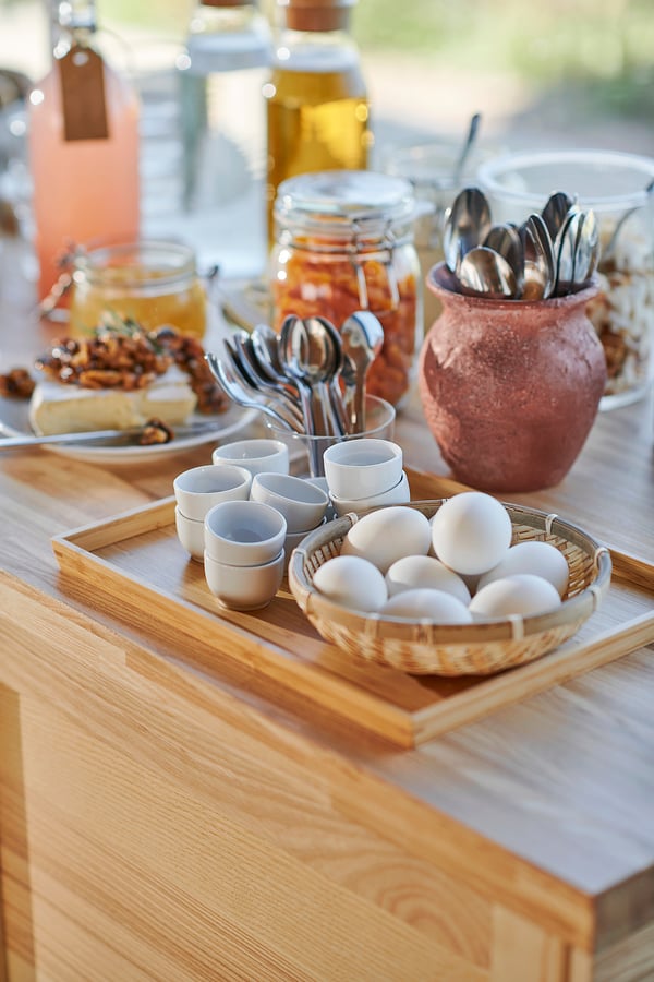 Breakfast tray with bowls, cups, jars, spoons on wooden table.