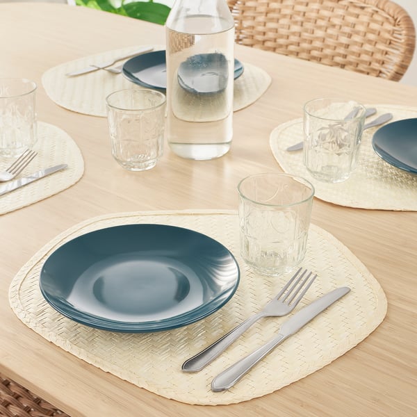 Wooden table set with blue plates, cutlery, glass cups, and woven place mats.