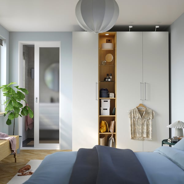 Modern bedroom with blue bed, PAX wardrobe, glass shelves, pendant light, and plant.