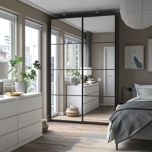Bedroom a PAX wardrobe with sliding doors, white drawers, a bed, and wooden floor. A mirror reflects the room.