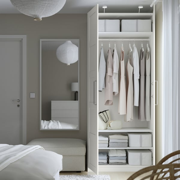 Open wardrobe with clothes, boxes, and a bench inside a bedroom.