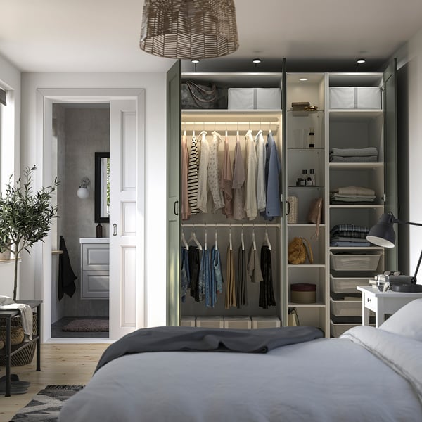 Well-organized bedroom with a PAX wardrobe featuring clothes hangers, shelves, and integrated lighting. A bed is partially visible in the foreground.
