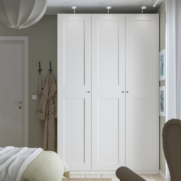 Minimalist bedroom with large white PAX wardrobe, silver knobs, grey door, and partially visible bed.