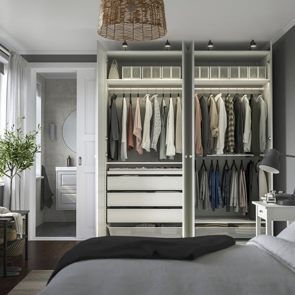 A modern bedroom with a large PAX wardrobe, showcasing organized clothing, drawers, and integrated lighting.