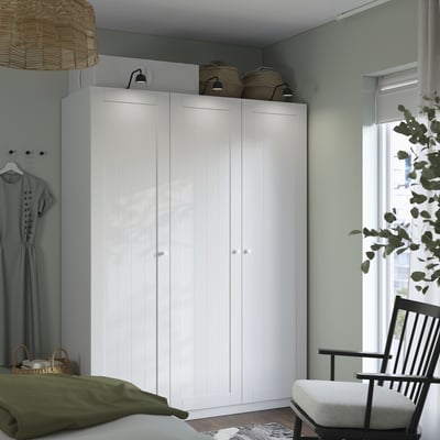 Modern bedroom with white PAX wardrobe, grey chair, woven baskets, and dress near window.