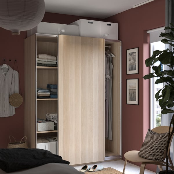 Modern bedroom with wooden PAX wardrobe, sliding doors, shelves with clothes, red walls.