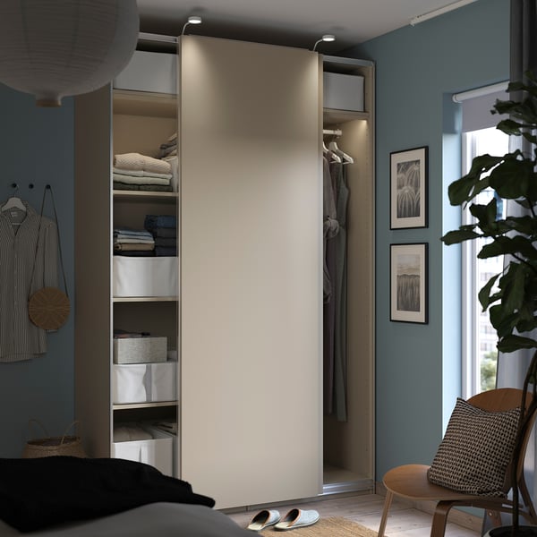 Modern bedroom with open PAX wardrobe in beige. Folded clothes, boxes, hangers, and sliding door.