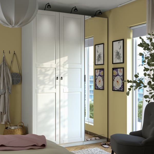 White PAX wardrobe with mirrors, beside armchair, holding bag & scarves, floral art.