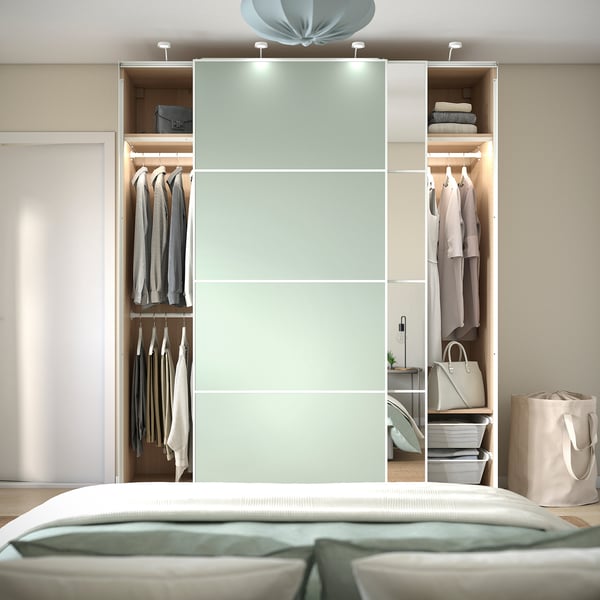 Modern bedroom with PAX wardrobe featuring sliding doors, hanging clothes, shelves with folded items, and integrated lighting.