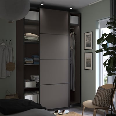 Modern bedroom with dark grey PAX wardrobe, sliding doors, and wooden chair. Decorated with plants and art.
