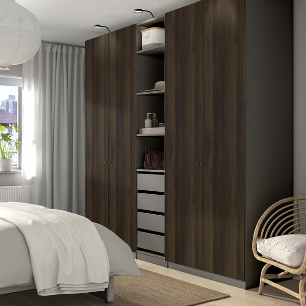 Modern bedroom with large dark wood wardrobe, made bed, wicker chair, and large window with sheer curtains.