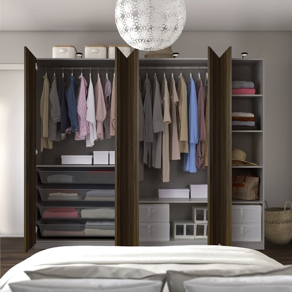 A well-organized, open wardrobe displaying hangers with clothes, shelves, and storage boxes. White lamp above, bed in front.