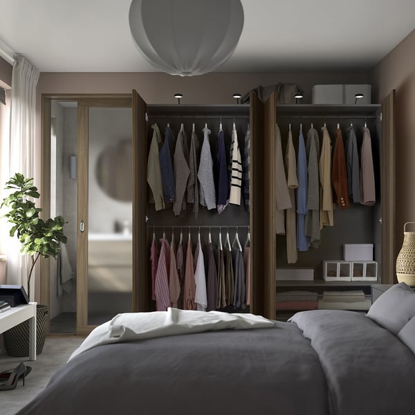Neat bedroom with open wardrobe showing clothes, featuring mirrored doors and wall-mounted lights.