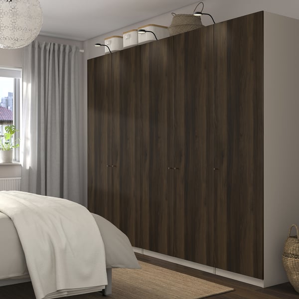Bedroom with dark wooden PAX wardrobes, mesh baskets, soft-close hinges, and decorative lights. Bed partially visible.