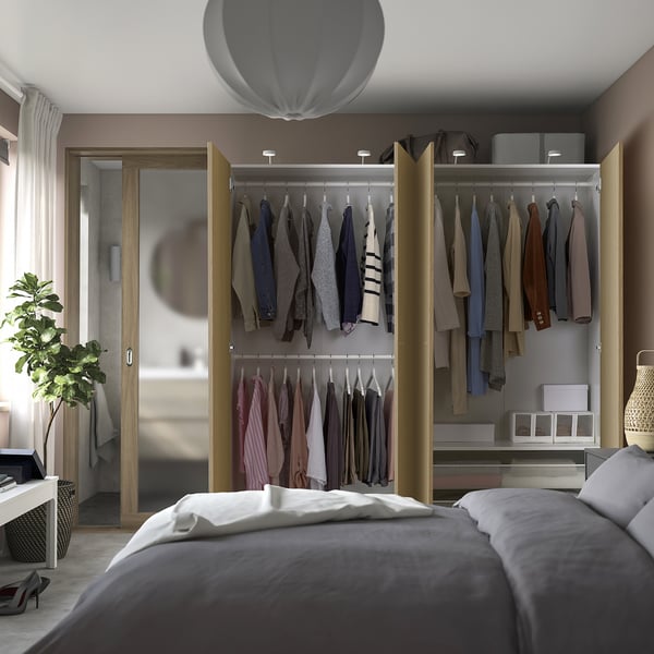 Bedroom with open wardrobe displaying clothes, featuring lit shelves and drawers.