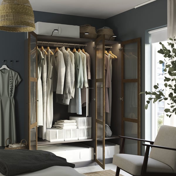 Modern closet with glass doors, lit interior, hanging clothes, shelves, and storage boxes.