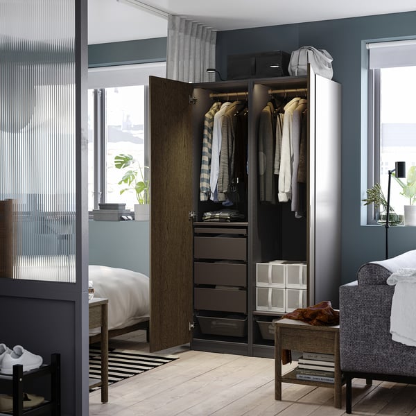 Modern bedroom with open wardrobe showing clothes, drawers, and organisers. The PAX wardrobe adjustable feet and integrated lighting.