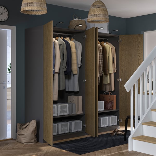 Closed PAX wardrobe displaying organised clothes and accessories with clear containers; set near staircase with woven pendants above.