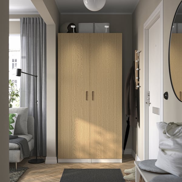 Oak wardrobe, tall with doors, lamp, curtain, seating, mirror, coat rack, dark rug.