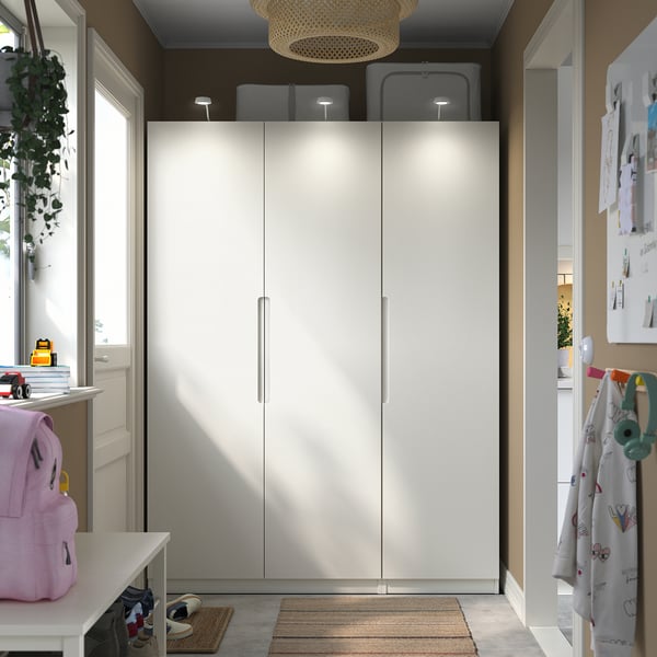 White PAX wardrobe with closed doors and bright lighting, flanked by a backpack and coat rack.