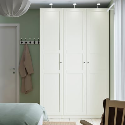 Large white PAX wardrobe with dark hooks, light-colored wall, hanging coat.