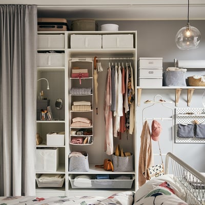Organised bedroom with white PAX wardrobe, shelves, drawers, and hanging space. Grey curtain and wood for warmth.