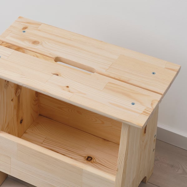 Simple wooden stool with open storage beneath. Light pine wood, natural finish. Handle cutout on top for easy moving.