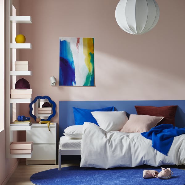 Modern bedroom: blue bed with white covers, pink walls; abstract painting, open shelves.