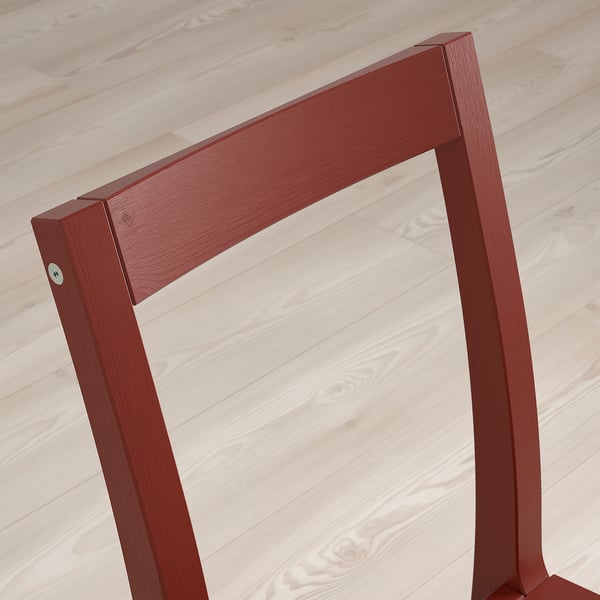 Red wooden chair backrest on light wooden floor. Solid, minimalist design.