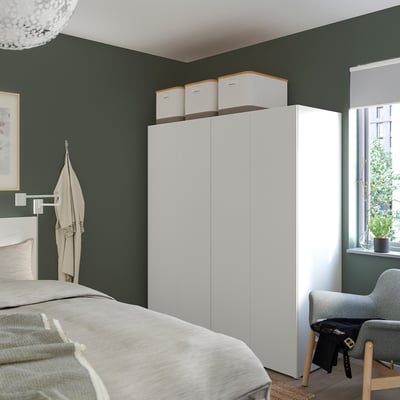 Modern bedroom with white PLATSA wardrobe against green wall, multiple compartments, larger than bed, cubes, coat rack, grey chair.