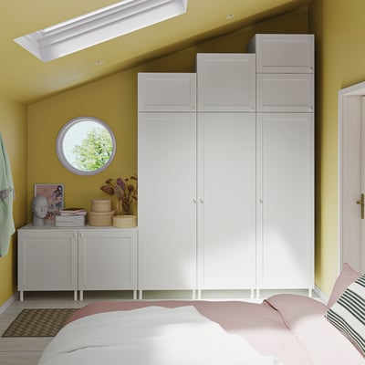 Modern bedroom with white PLATSA wardrobe, side cabinet, and bed in yellow room.