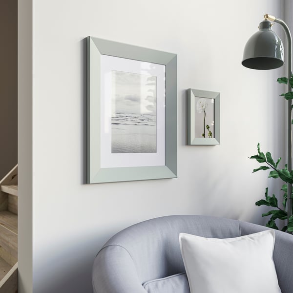 Minimalist room with grey frame, beach photo, blue armchair, green leaves, black lamp.