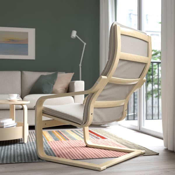 A stylish light wooden armchair with a beige cushion near a window, beside a colourful rug in a cosy living room.