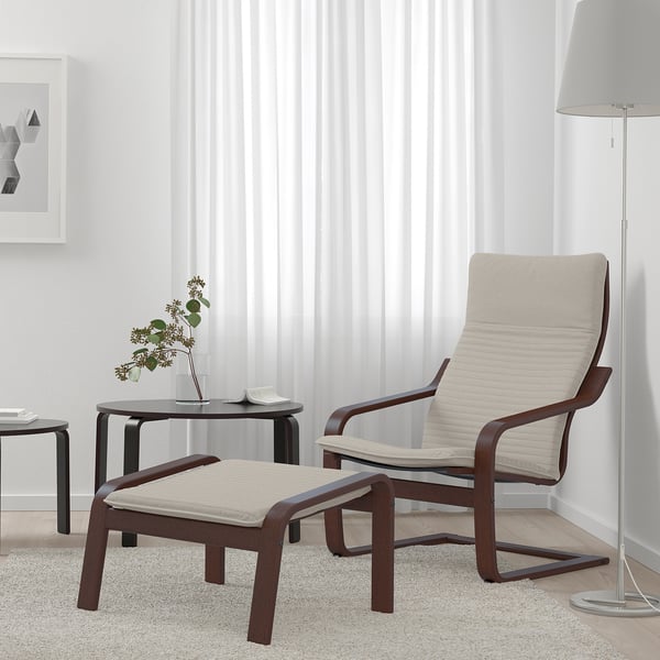 Modern living room with beige POÄNG chair, footstool, dark wood trim, side table with flowers, and floor lamp by window.