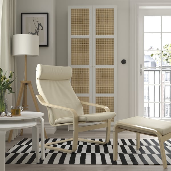 Stylish living room with POÄNG armchair, footstool, side table, lamp, striped rug, canvas print, and large window.