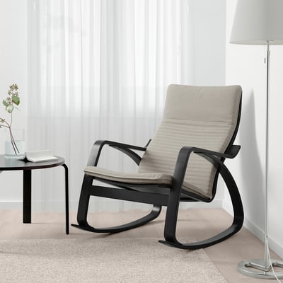 Modern living room with beige POÄNG rocking chair on patterned rug, beside small table with plant and floor lamp.