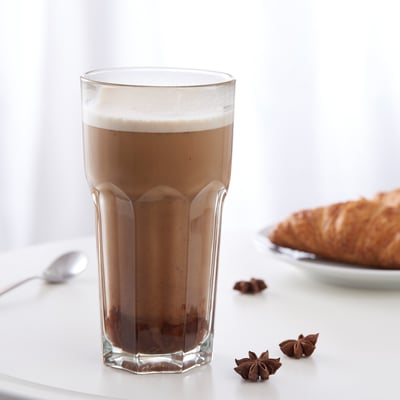 A tall glass of frothy iced coffee on a table with a spoon and star anise spices.