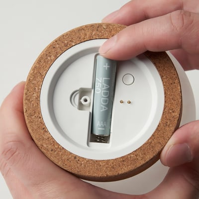 Hand placing an aaa battery into a reusable lamp, highlighting the easy battery replacement feature.