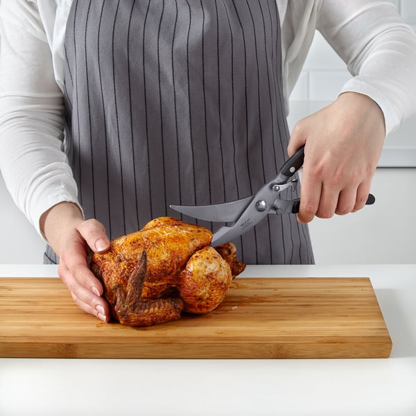 A person using shears to cut a roasted chicken on a cutting board.