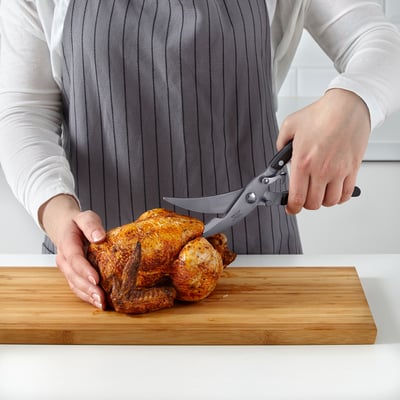 A person using shears to cut a roasted chicken on a cutting board.