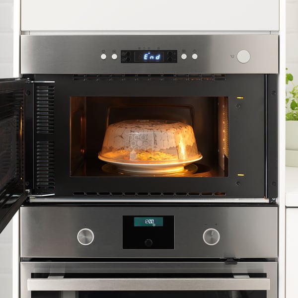 Built-in microwave oven with a digital display and a heating dish inside covered with a lid.