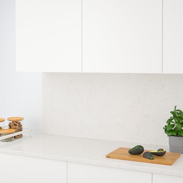 Clean modern kitchen with quartz countertop and backsplash, avocados, bread, and plant on a cutting board.