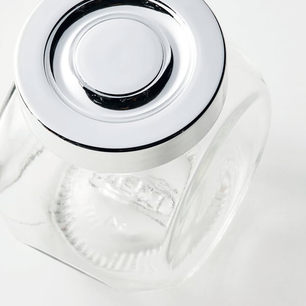 Clear glass jar with metallic lid, reflecting light, sits on white surface.