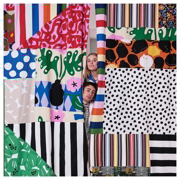 Two people behind colourful patterned fabric rolls.